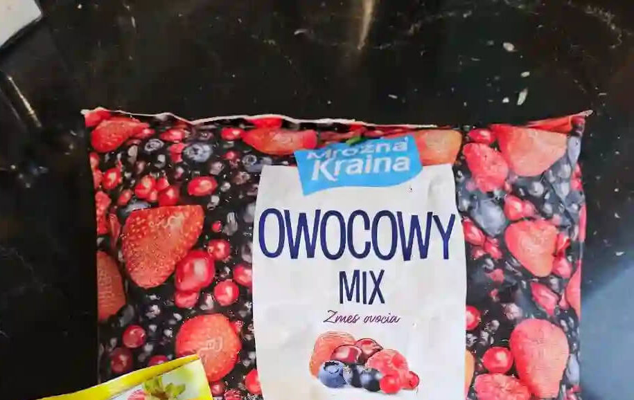 Składniki na sernik: Mrożone Owoce Opakowanie mrożonego "Owocowego Mixu" (truskawki, borówki, maliny) i torebka galaretki truskawkowej WINIARY, przygotowane do użycia.