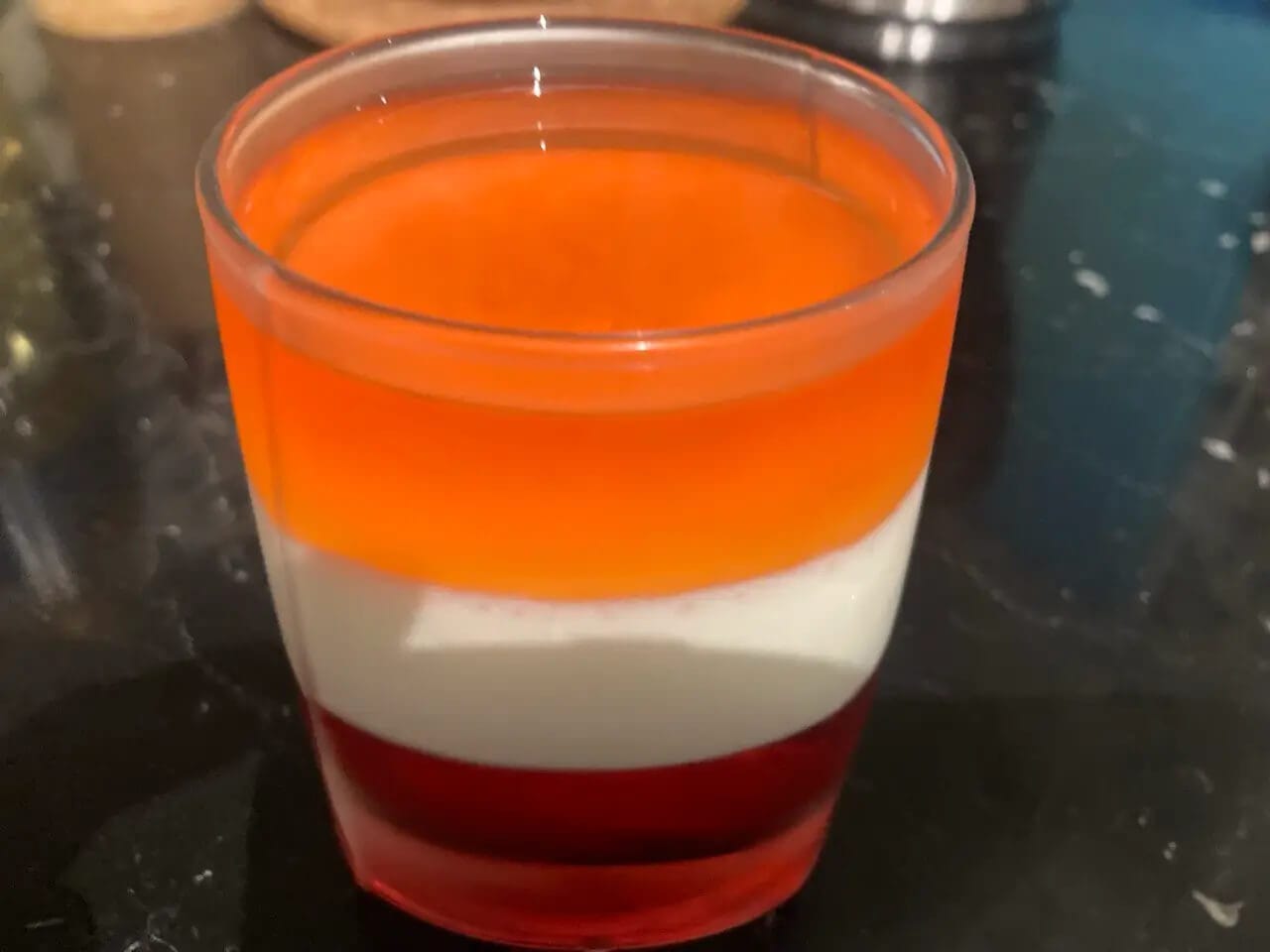 Deser warstwowy w szklance - czerwony, biały i pomarańczowy galaretka lub panna cotta