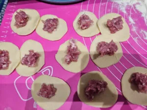 Nakładanie farszu roślinnego na okrągłe kawałki ciasta bezglutenowego na różowej macie. Pierogi z nadzieniem roślinnym