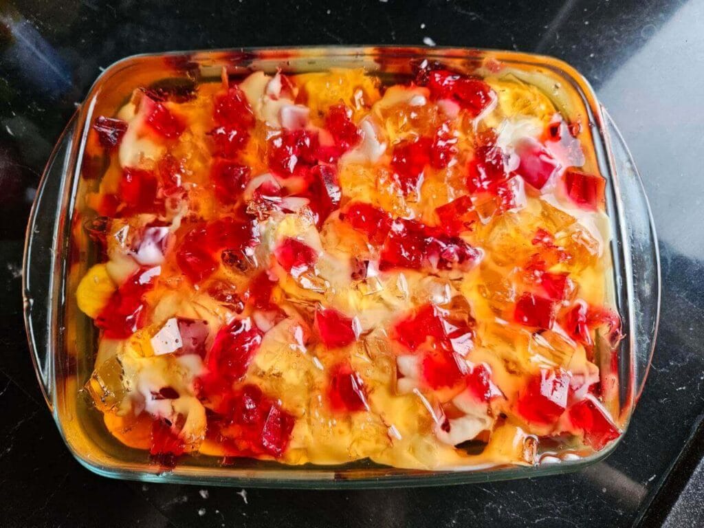 Broken glass cake in a glass baking dish with red and orange jelly cubes.