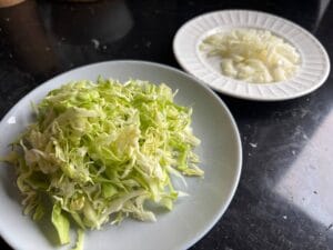Poszatkowana biała kapusta i pokrojona cebula jako pierwszy krok przepisu na danie kapusta zasypana.