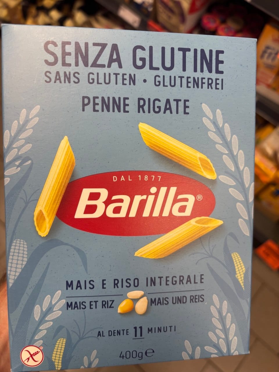 Jasnoniebieskie opakowanie bezglutenowego makaronu Barilla Penne Rigate z kukurydzy i brązowego ryżu, z grafiką rurek makaronowych oraz symbolem Przekreślonego Kłosa.