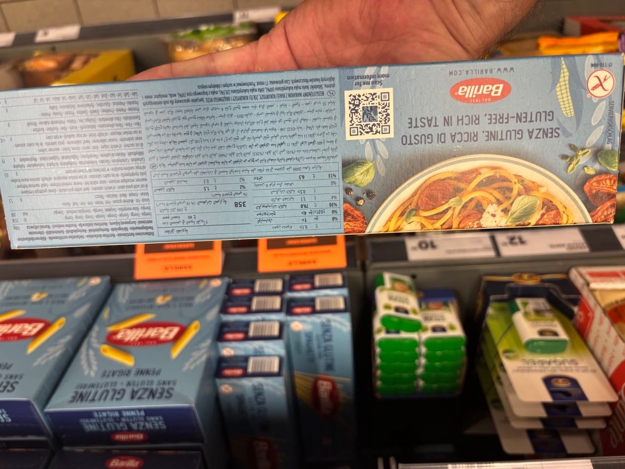 Odwrócone opakowanie makaronu Barilla Senza Glutine Spaghetti przedstawiające tabelę wartości odżywczych, wielojęzyczny skład, kod QR oraz grafikę gotowego dania z makaronem. Produkty bezglutenowe w Netto.