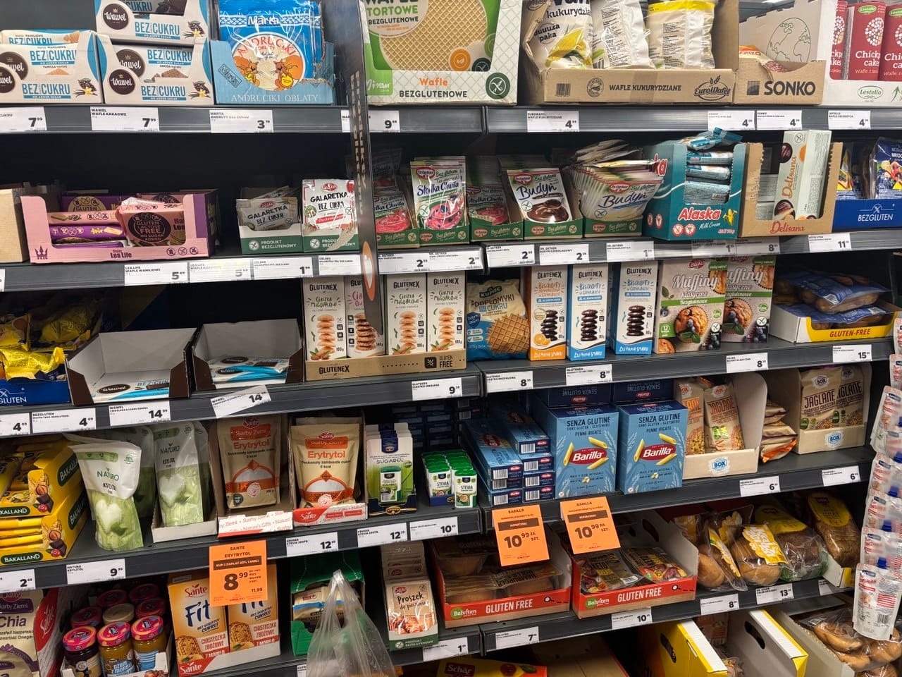 Półka sklepowa w Netto pełna produktów bezglutenowych, w tym wafli, budyni, galaretek, ciastek i makaronów Barilla ze znakiem Przekreślonego Kłosa. Produkty bezglutenowe w Netto.