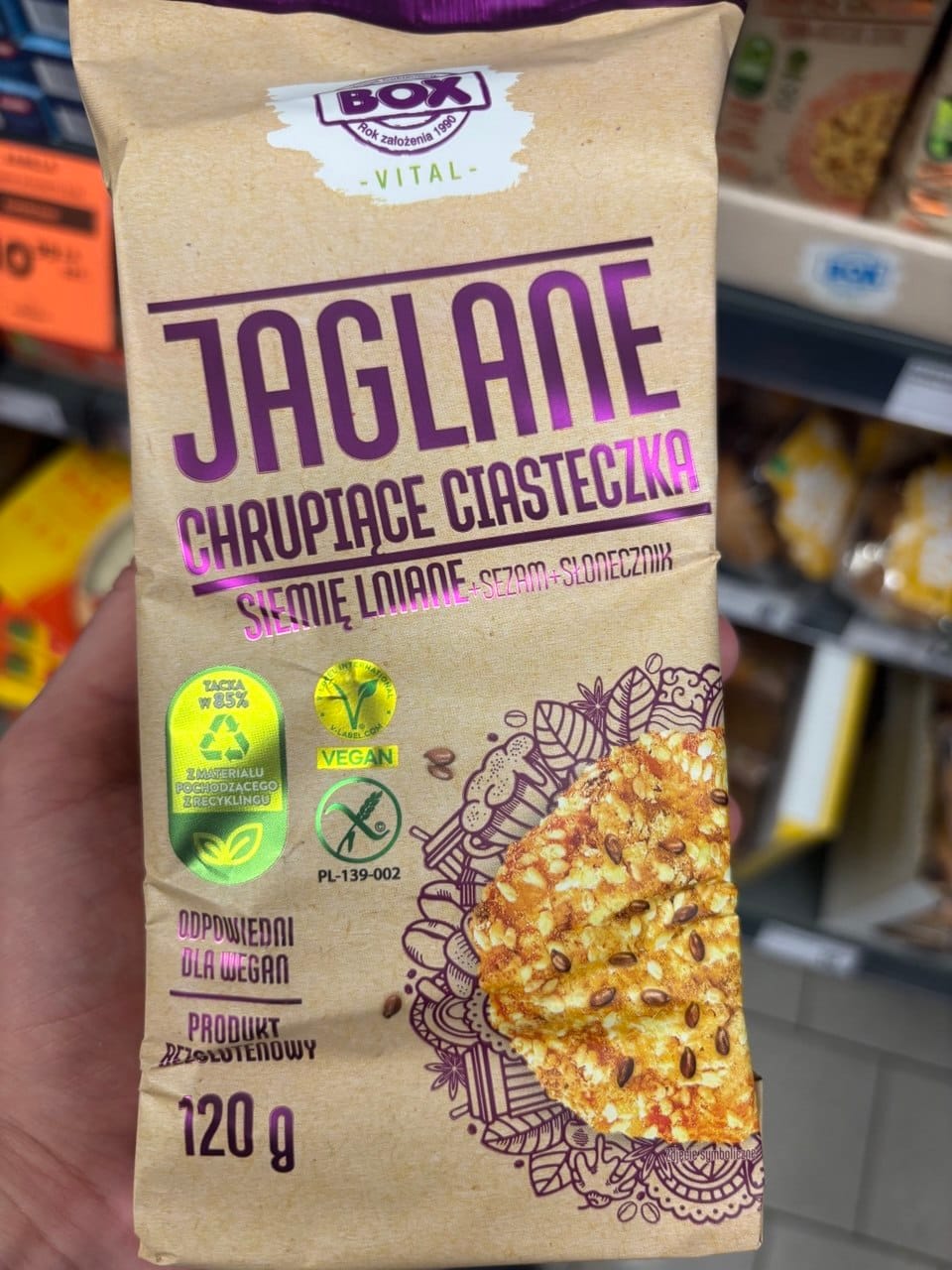 Papierowe opakowanie ciasteczek jaglanych Box Vital Jaglane chrupiące ciasteczka z siemieniem lnianym, sezamem i słonecznikiem, o wadze 120 g, z widocznym symbolem Przekreślonego Kłosa oraz znakiem Vegan. Produkty bezglutenowe w Netto.