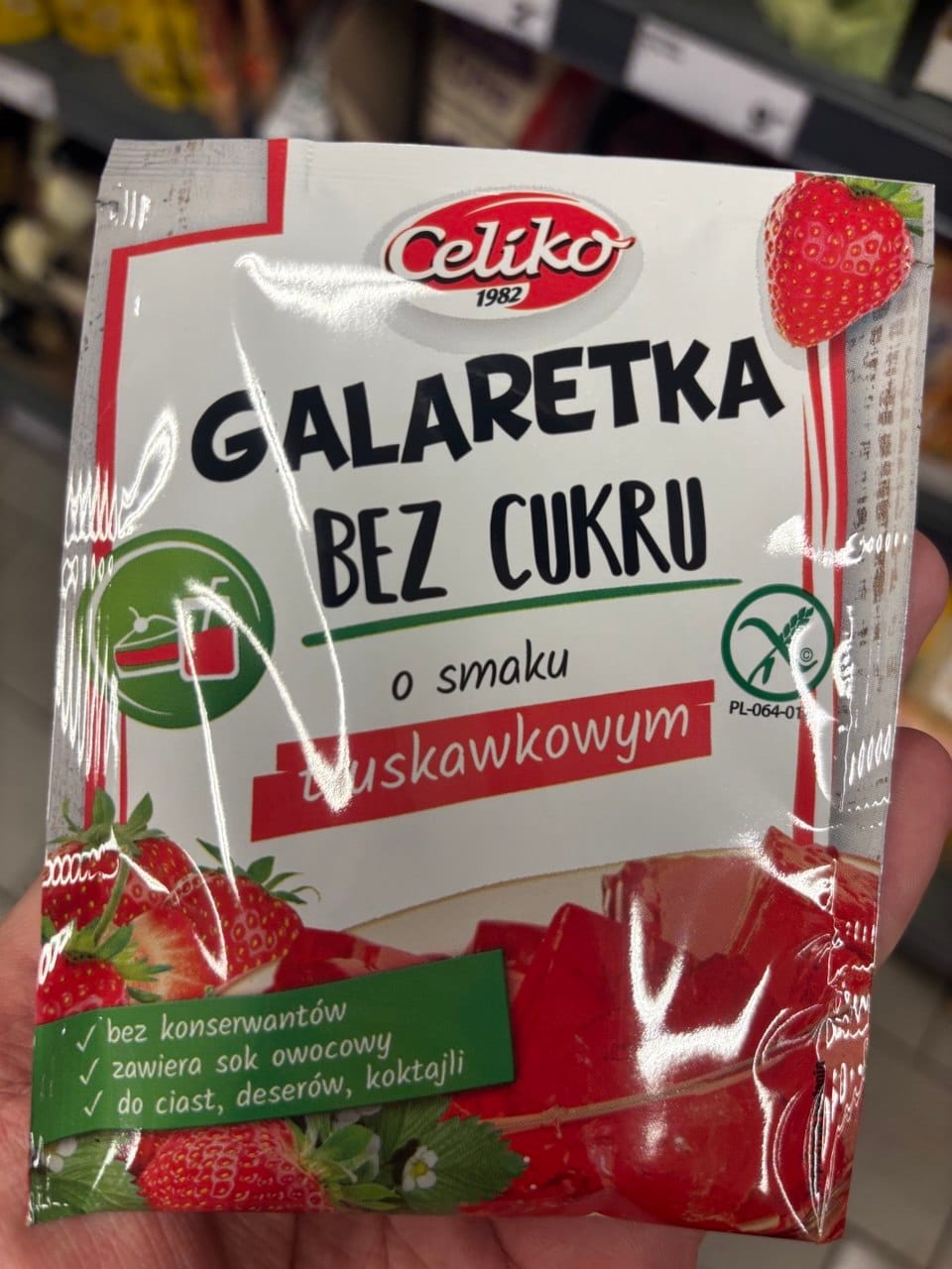 Opakowanie truskawkowej galaretki bez cukru Celiko z soczystymi grafikami truskawek, czerwonych kostek deseru oraz okrągłym znakiem Przekreślonego Kłosa.