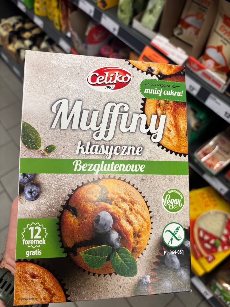 Kartonowe opakowanie mieszanki Celiko Muffiny klasyczne Bezglutenowe z grafiką babeczki z borówkami, zielonym symbolem Przekreślonego Kłosa oraz znaczkiem Vegan.
