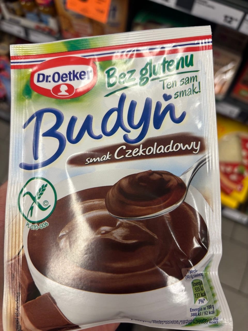 Opakowanie bezglutenowego budyniu czekoladowego Dr. Oetker Budyń smak Czekoladowy z grafiką miseczki kremowego deserzu та symbolem Przekreślonego Kłosa. Produkty bezglutenowe w Netto.