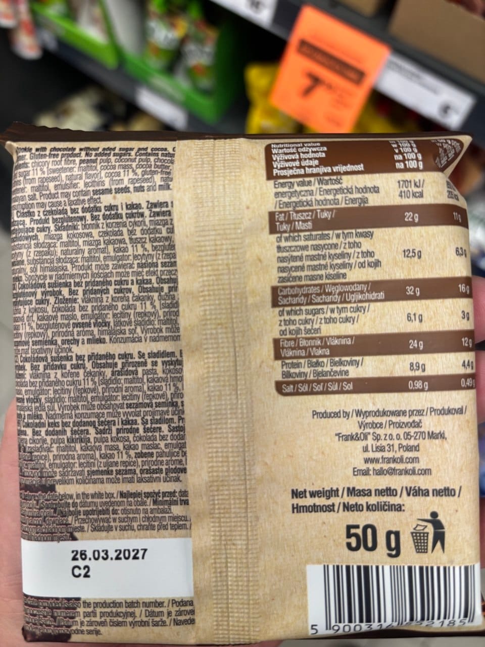 Odwrócona strona opakowania ciastka Frank & Oli Brownie, przypominająca strukturą ekologiczny, jasnobrązowy papier. Po prawej stronie wyraźnie odznacza się duża, minimalistyczna tabela z wartościami odżywczymi, podająca m.in. 410 kalorii w stu gramach, a na samym dole widnieje pogrubiona waga netto 50 g oraz czarny kod kreskowy. Po lewej stronie gęsty blok tekstu szczegółowo opisuje bezglutenowy skład i ostrzeżenia dla alergików w kilku językach.