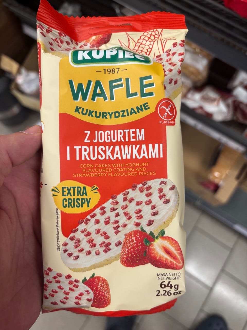Opakowanie wafli kukurydzianych Kupiec z polewą jogurtową i liofilizowanymi truskawkami. Na opakowaniu widoczne są świeże truskawki, wafle oraz symbol Przekreślonego Kłosa. Produkty bezglutenowe w Netto.