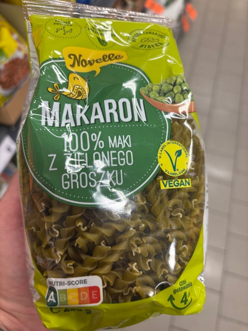 Opakowanie zielonego makaronu świderki Novelle Makaron 100% z mąki z zielonego groszku, z widocznym żółtym certyfikatem Vegan V-Label oraz oznaczeniem Nutri-Score A. Produkty bezglutenowe w Netto.