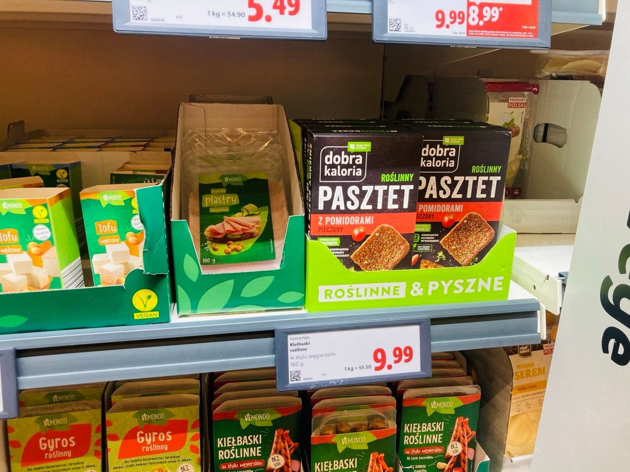 Wegańskie produkty w supermarketach Lidl: pasztet Dobra Kaloria, wegańskie kiełbaski Vemondo i tofu na półce sklepowej.