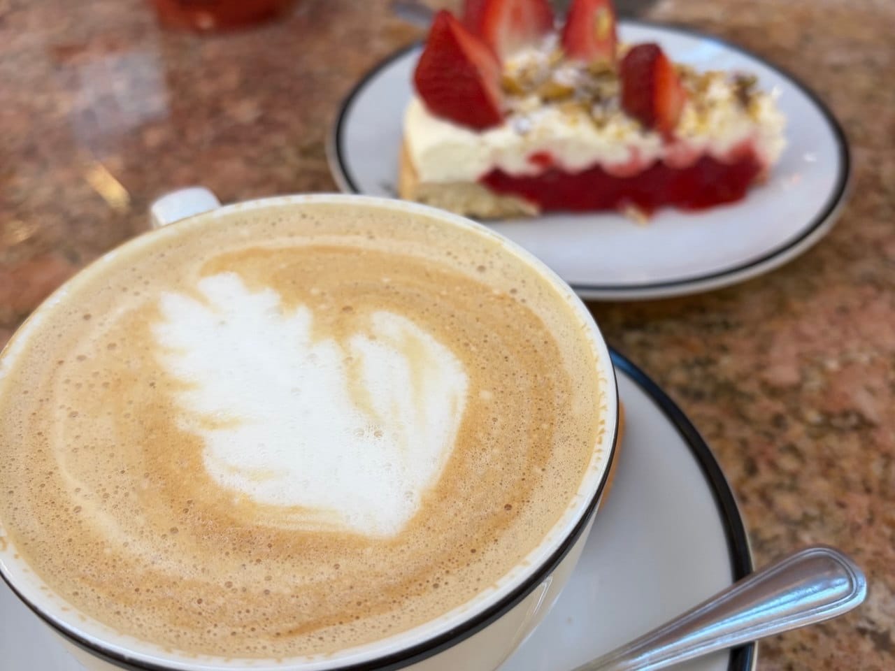 Filiżanka kawy z latte art i bezglutenowe ciasto truskawkowe na talerzyku w tle