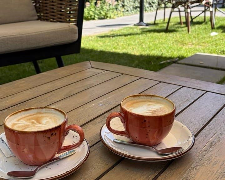 Two reddish cups of plant-based cappuccino on a wooden table at a gluten-free friendly outdoor cafe in San José, Costa Rica.