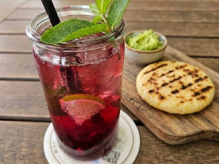 Traditional gluten-free and vegan corn arepa served with fresh guacamole and a fruit drink in Colombia