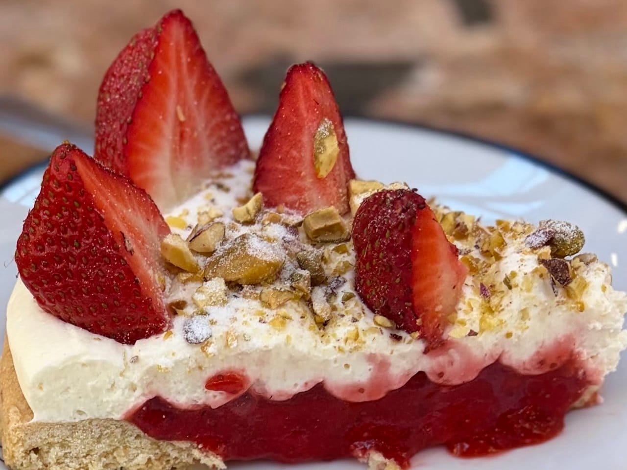 A slice of gluten-free and vegan strawberry cake topped with plant-based cream, fresh strawberries, and crushed nuts, served at a cafe in Bulgaria.