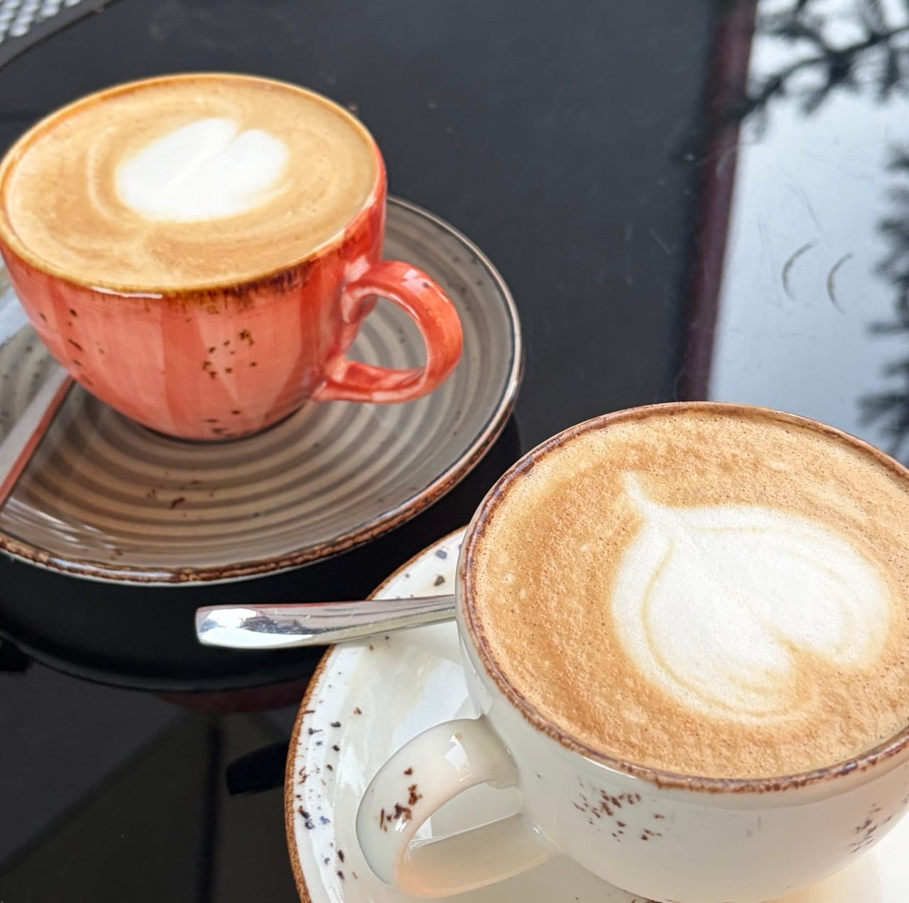 Two cups of vegan coffee with latte art on a dark glass table at a cafe in Skopje, North Macedonia.