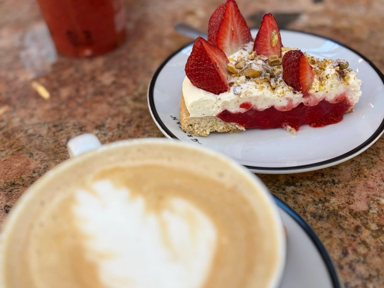 A slice of gluten-free and raw vegan strawberry tart with dairy-free cashew cream and a nut crust, served with plant-based coffee at a bakery in Budapest.