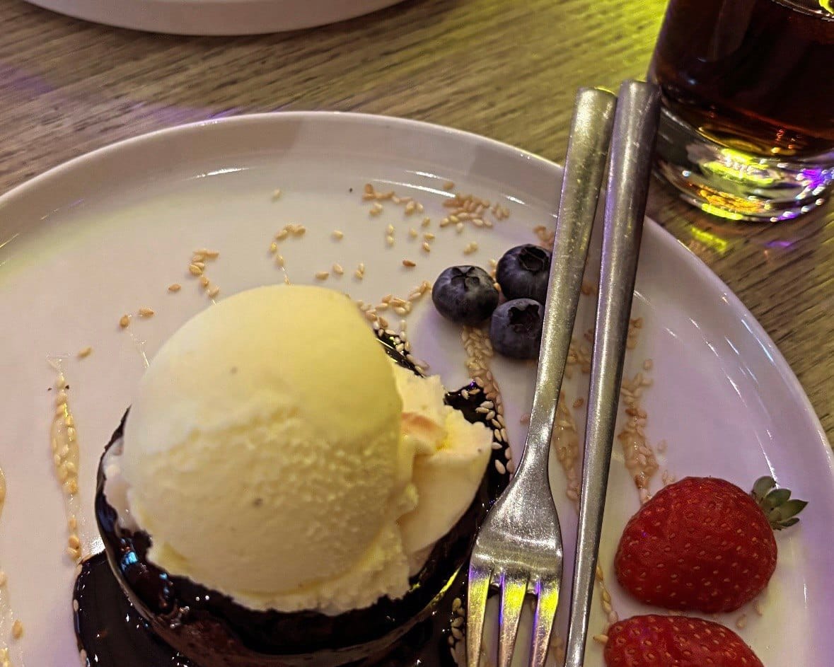 A gluten-free chocolate brownie topped with a scoop of vegan vanilla ice cream and fresh berries on a white plate in Tallinn.