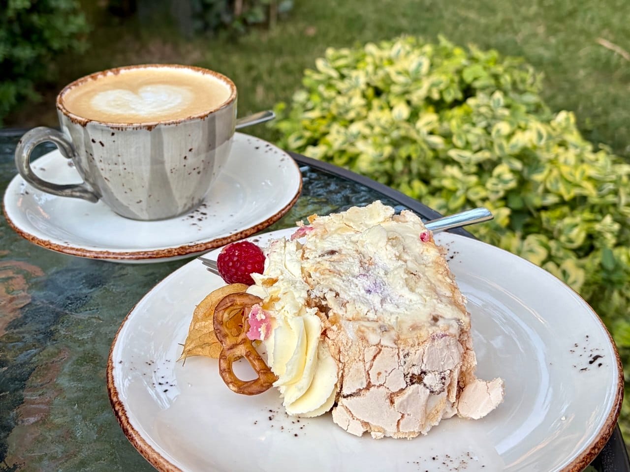 A slice of gluten-free and vegan meringue cake with a pretzel next to specialty coffee at a cafe in Belgrade, Serbia.