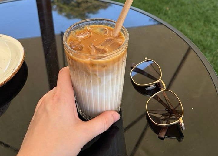 A hand holding a glass of vegan iced coffee made with coconut milk at an outdoor cafe in Vietnam.