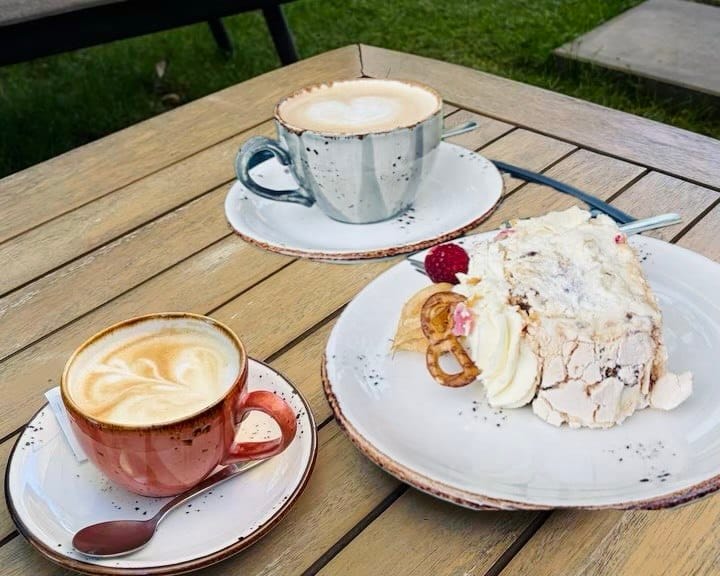 Kawa z latte art i bezglutenowa beza na drewnianym stole – słodka Lizbona bez glutenu.