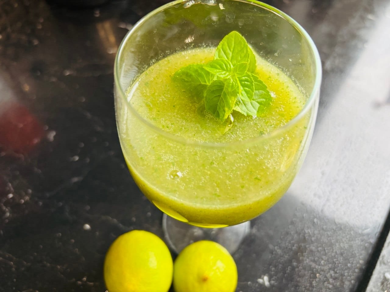 Zielonkawy napój z pepino i jabłka w szklance na nóżce z miętą i limonkami