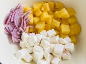 Pokrojone pepino, wegańska feta i czerwona cebula w misce przed wymieszaniem sałatki