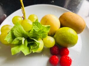 Świeże owoce na talerzu: winogrona, pepino, kiwi, limonka i maliny z miętą