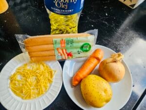 Składniki na wegańską zupę: sojowe parówki, ziemniak, marchew, cebula i makaron na blacie.